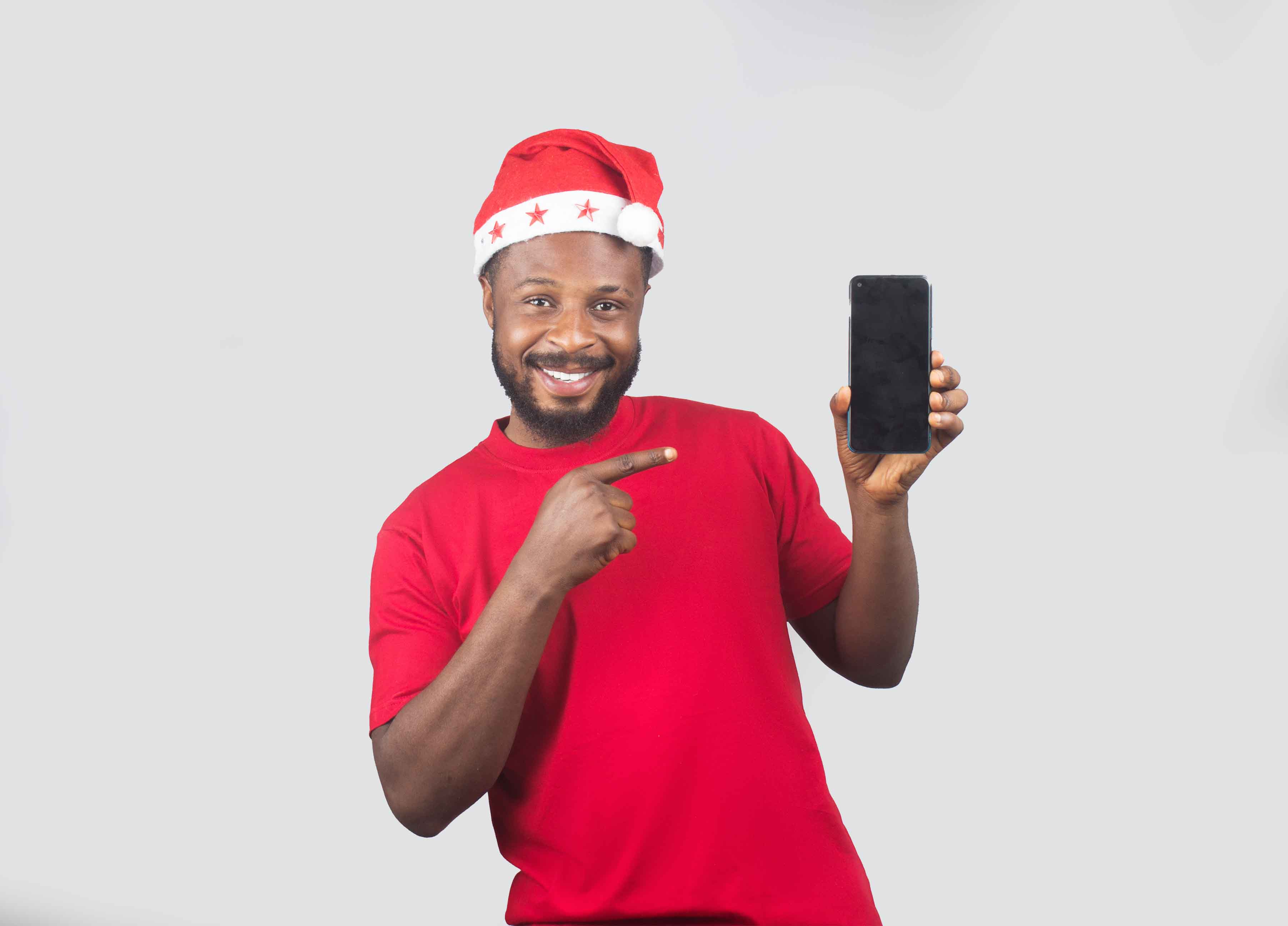 An African Nigerian man wearing a Christmas cap, holding a phone in one hand and pointing at it with the other hand 3.